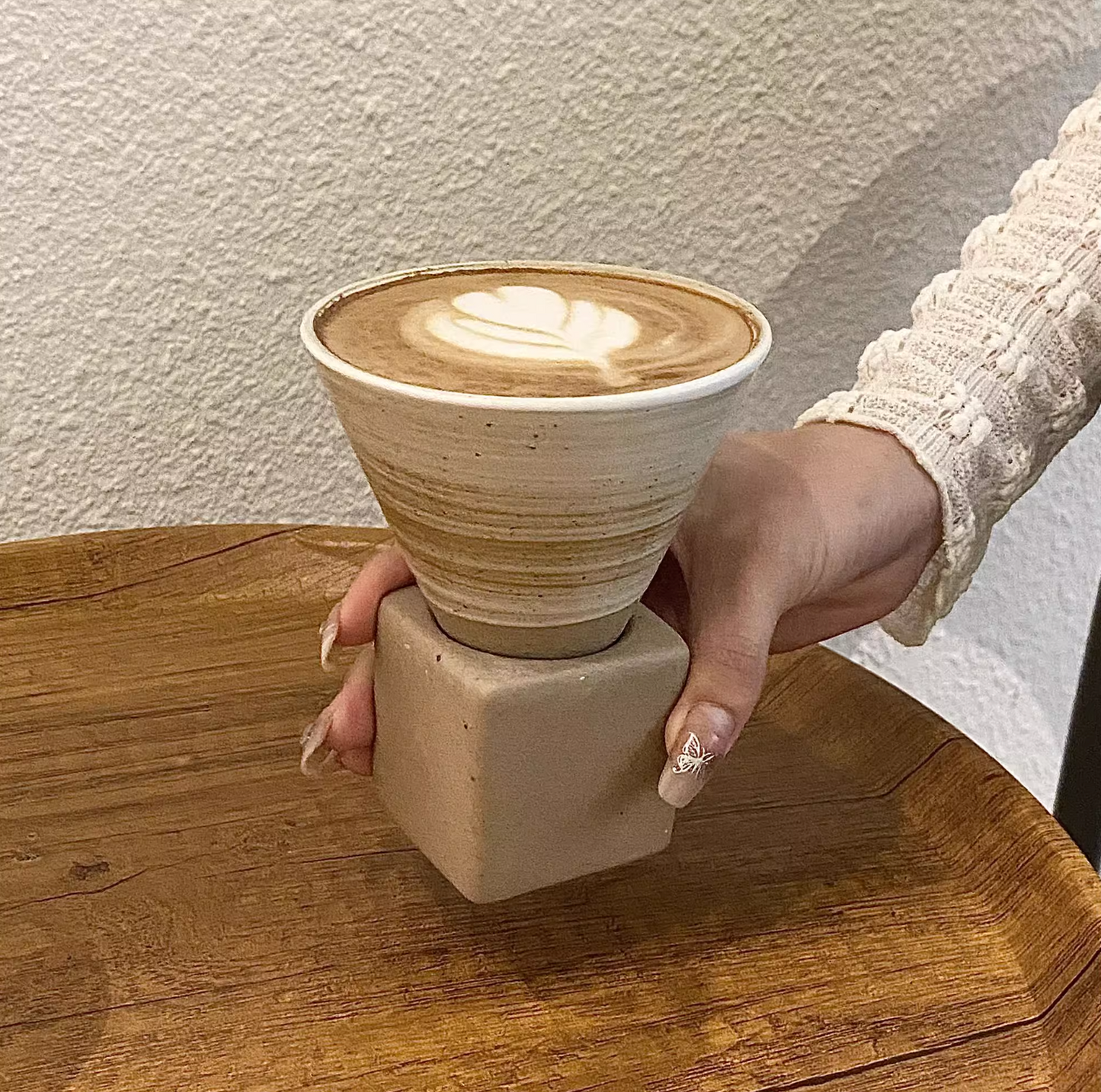 Ceramic cone-shaped cup with a handle held by a hand on a wooden surface