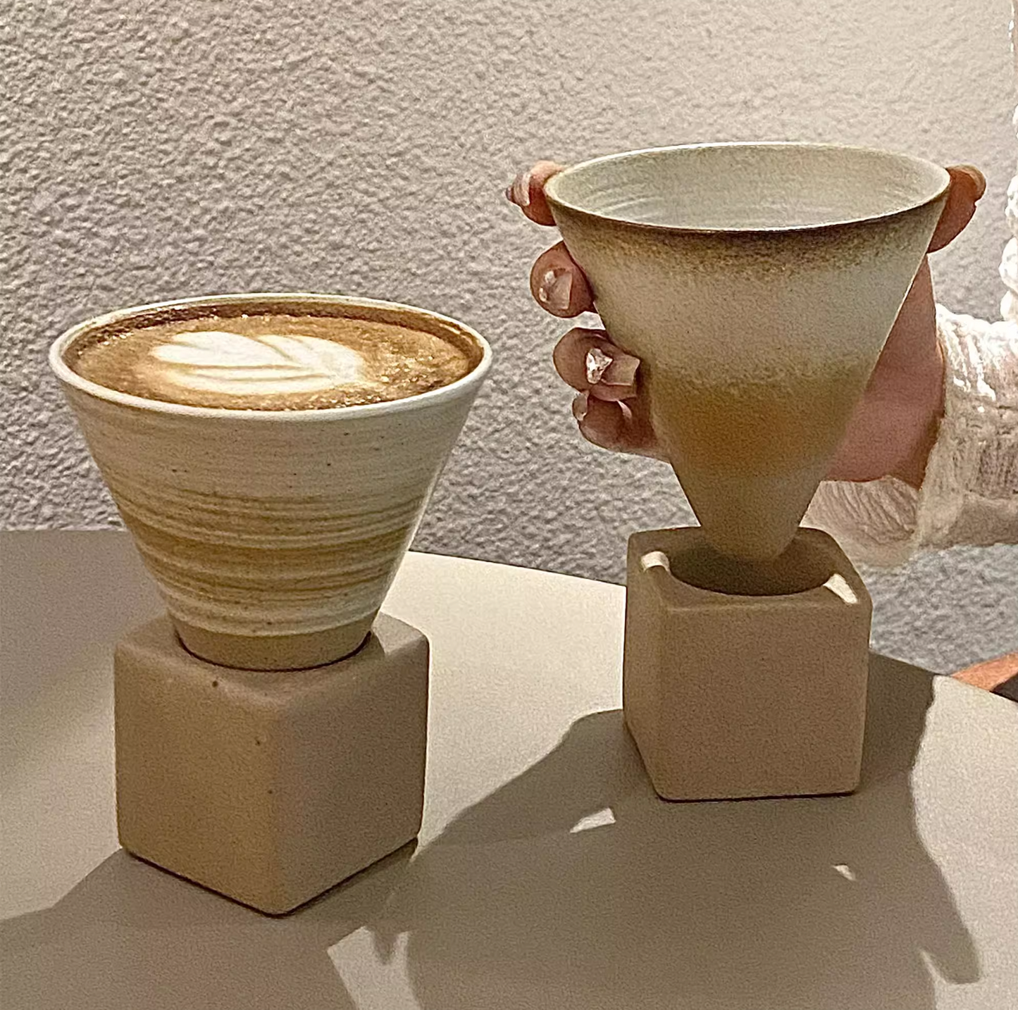 Two ceramic cone-shaped cups with a textured finish on a light surface.