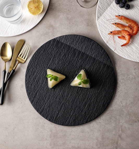 Two triangular appetizers on a black slate board with silverware and a dish of shrimp in the background.