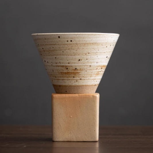 Ceramic cone-shaped coffee mug on a ceramic block against a dark background