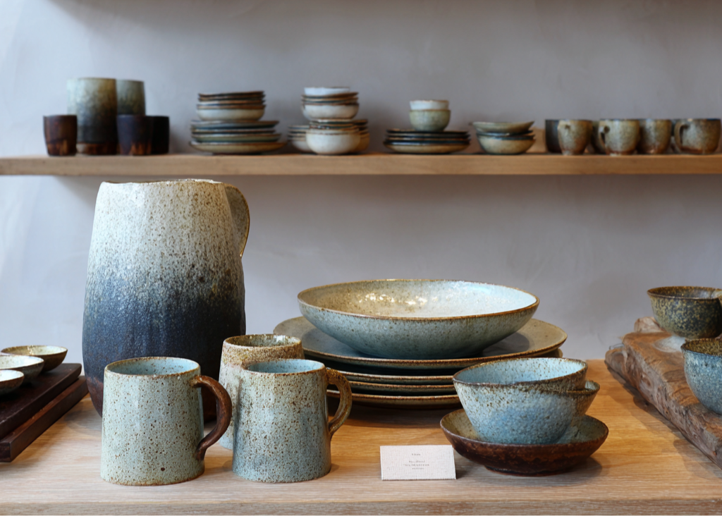 Collection of ceramic dishes on wooden shelves against a neutral wall.