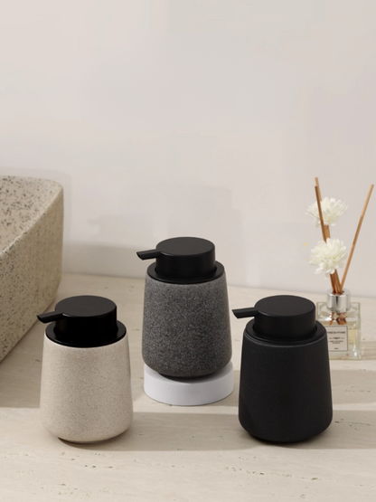 Three cylindrical soap dispensers in black, gray, and white on a bathroom counter.