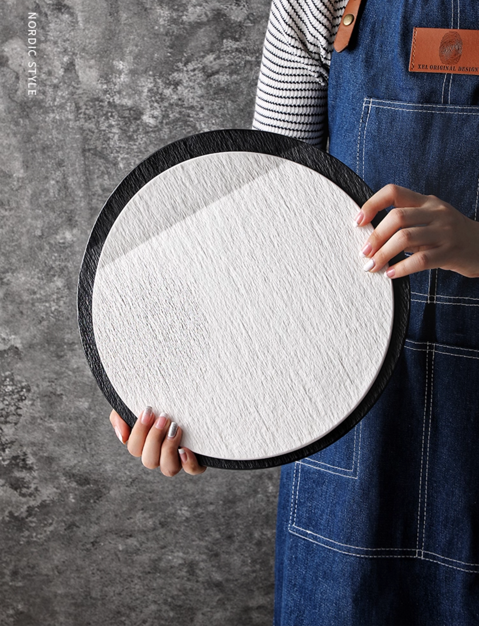 Person holding a round white and black plates against a gray textured background